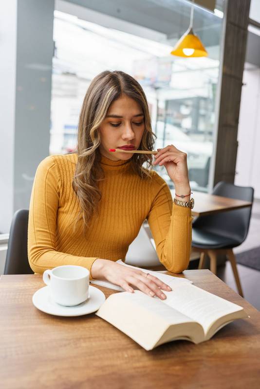 attractive young latin woman with blonde hair sitting at a table concentrated reading a book