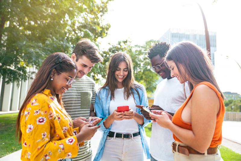 happy young friends looking mobile phone and smiling - five happy teenagers with a smartphone - Lifestyle concept