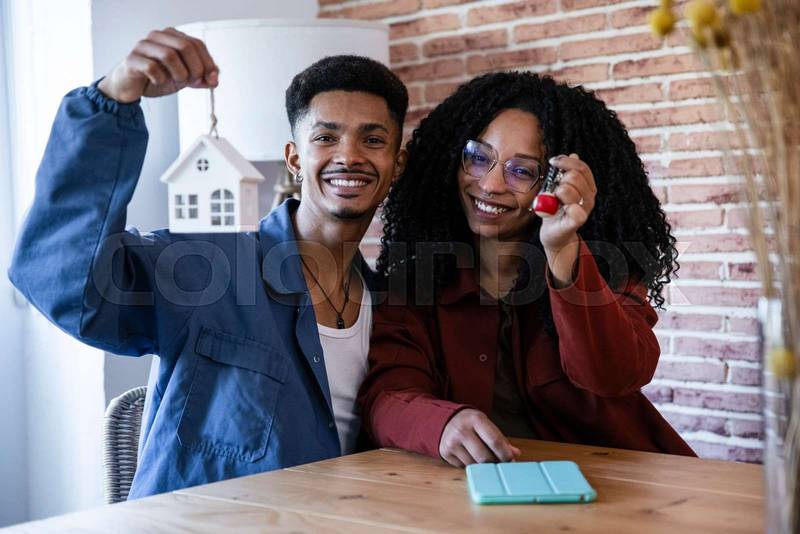 Satisfied man and woman smiling and holding keys of a property in a living room. Joyful couple celebrating buying new home showing keys and looking at camera. 