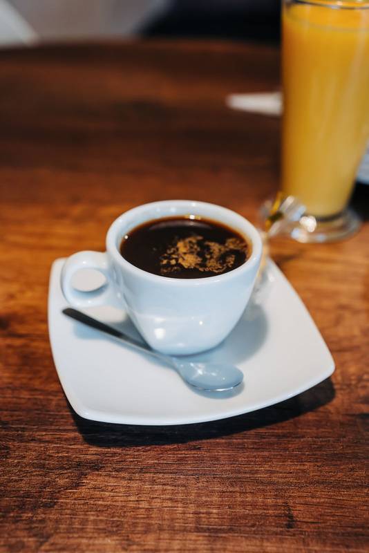 cup of coffee with cream, saucer on wooden table, hot caffeinated drink