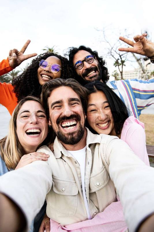 Vertical portrait of a diverse group of friends taking a selfie in the street. Cheerful multiracial group of young hipsters taking a picture outside and looking at camera.