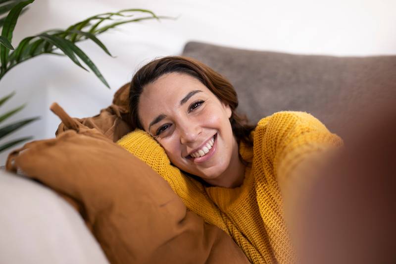 Close-up young cheerful woman looking at camera taking a selfie. Beautiful smiling female taking a selfie with smartphone while relaxing at home.
