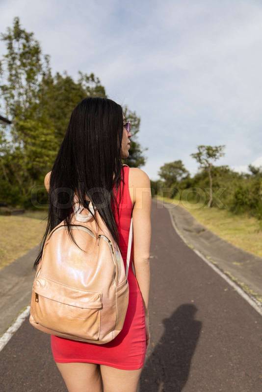 walking on asphalt road, wearing red casual dress and backpack, tourist