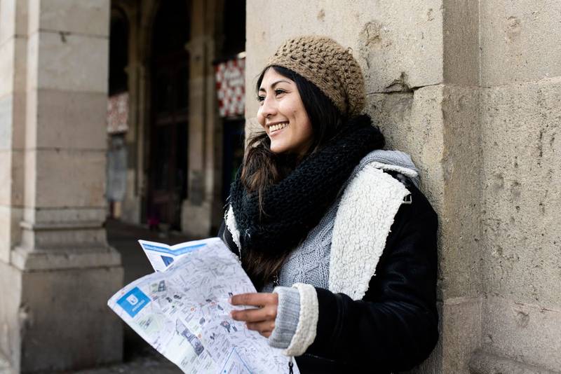 young tourist woman exploring city map in the street. holidays, tourism and travel concept
