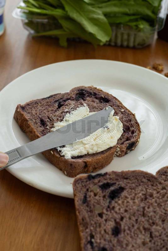knife spreading creamy cheese on a fresh slice of bread, snack