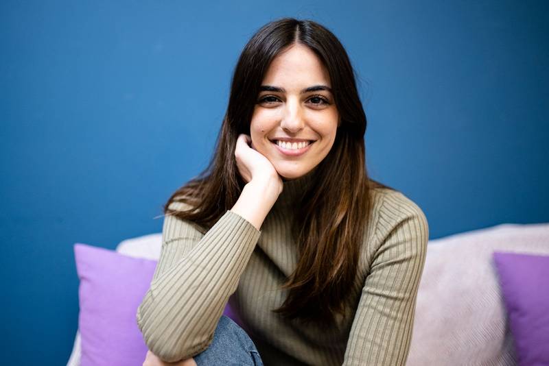 Happy young woman sitting on sofa at home and looking at camera. Portrait of comfortable caucasian woman similing and relaxing on armchair