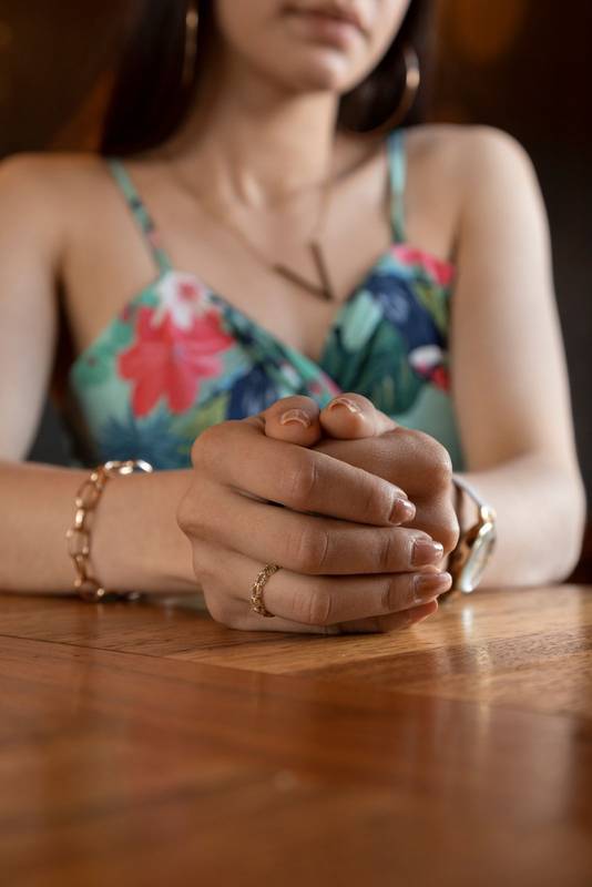 hands crossed, wearing a colorful top and jewelry