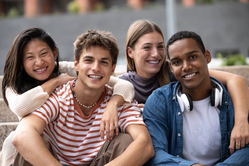 Beautiful young millennials smiling looking at camera.Group of friends sitting together happy and carefree in the street.