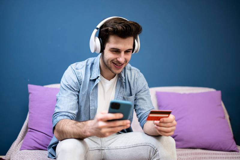 Man sitting in front of the computer holding a credit card at home - Young adult doing a online payment with his laptop at kitchen - business, technology concept